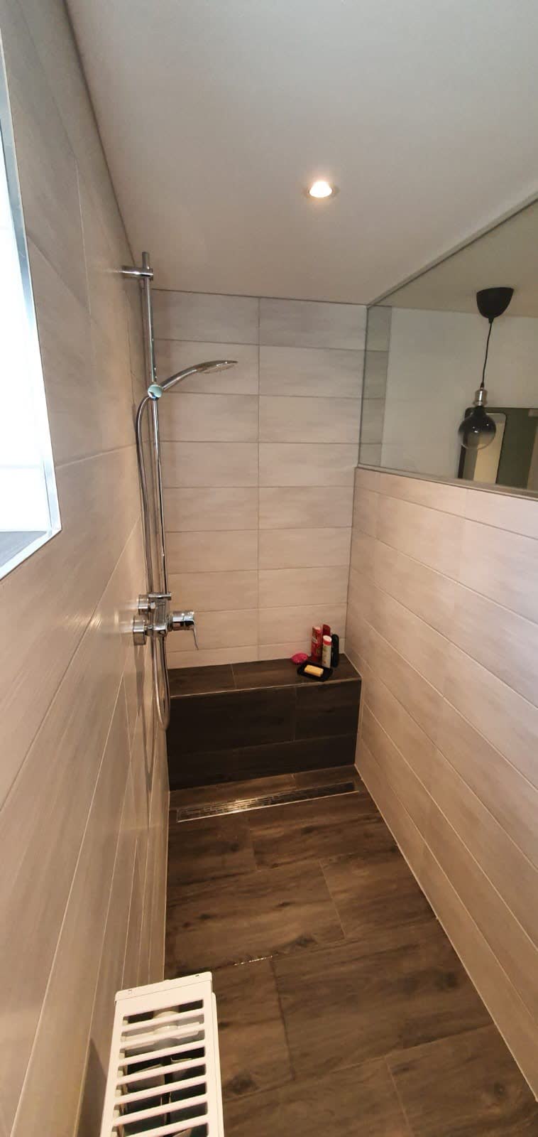 Fertig geflieste Dusche mit Sitzbank, hellen Wandfliesen und Bodenfliesen in Holzoptik